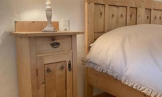 A cozy bedroom with a wooden bed and a bedside table. The lamp on the bedside table has a decorative lampshade.