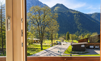 A view from a window onto a green landscape with mountains in the background. It is a clear, sunny day.
