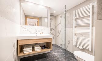 A modern bathroom with an elegant shower and a wooden washbasin. The walls are designed in a light, minimalist style.