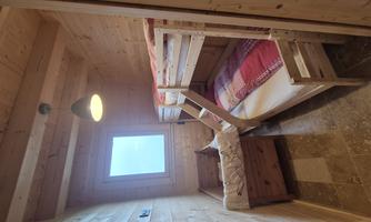 A small room with two bunk beds and a window. The walls are made of wood, and the floor is tiled.