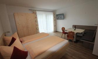 A cozy bedroom with two single beds and wooden furniture. The room has a dining area and large windows with plenty of daylight.