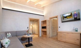A modern accommodation with a gray sofa and a small table. A television hangs on the wall, and there is light wood decor in the room.