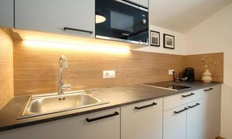 A modern kitchen with a stainless steel sink and a black countertop. It is well-lit with wood panels and has modern kitchen appliances.