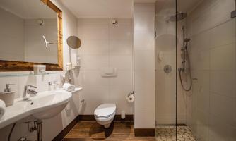 A modern bathroom with a shower and a sink. The walls are light and the floor has a wood look.