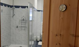 A modern bathroom with a shower and a bathtub. The walls are tiled in light colors, and a wood-colored door leads inside.