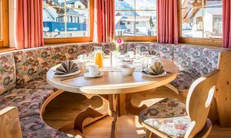 A cozy dining area with a round table and charming benches. Large windows provide plenty of daylight and a view outside.