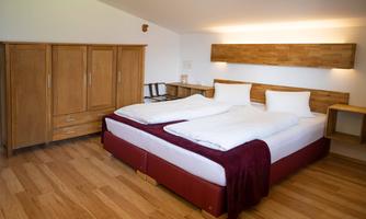 A modern bedroom with a large double bed and wooden flooring. The room is bright and furnished in a minimalist style, with a wardrobe and sideboard.