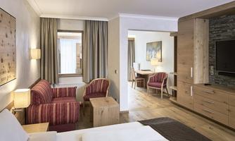 A modern hotel room with wooden decorations and comfortable furniture. There is a living area with a sofa and table, as well as a bedroom with a large bed.