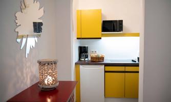 A modern kitchen with yellow cabinets and white walls. It is minimally furnished and features a microwave, a refrigerator, and a coffee maker.