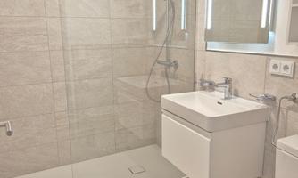 A modern bathroom with a glass shower and an elegant vanity combination. The walls are tiled in light colors and the room light is welcoming.