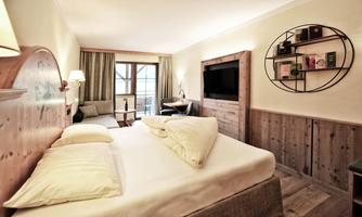A cozy hotel room with a double bed, a sofa, and a modern TV. The warm wooden decor creates an inviting atmosphere.
