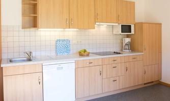 A modern kitchen with wooden cabinets and a bright workspace. It is well-equipped with a stove, sink, and dishwasher.