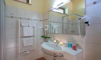 A modern bathroom with bright tiles and a sink. Towels, plants, and toiletries are visible.