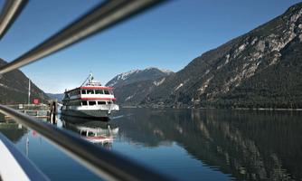 A beautiful boat lies quietly at the shore of a lake, surrounded by tall mountains. The sky is clear and blue, enhancing the peaceful atmosphere.