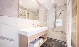 A modern bathroom with a large shower and an elegant sink. The walls are adorned with stylish marble and concrete.
