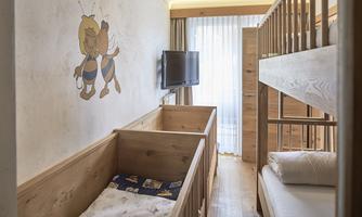 A cozy children's room with two wooden beds and a television. On the wall, there is a friendly illustration of a bee character.