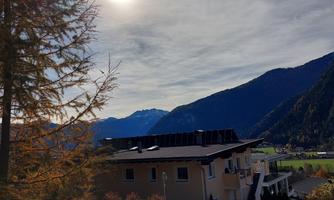 A house between mountains under a clear sky. The sun is high in the sky and shines onto the landscape.