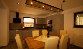 A modern kitchen with a large wooden table and elegant chairs. The walls are painted in neutral tones, and there is a practical kitchenette.