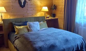 A cozy bedroom with a large bed and wood paneling. On the wall hang a deer antler and two bedside lamps.