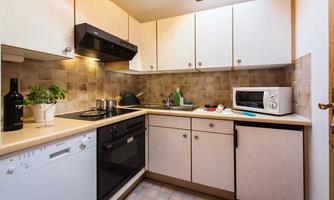 A modern kitchen with bright cabinets and a countertop. It is equipped with a stove, a microwave, and cooking utensils.