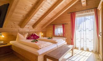 A cozy bedroom with wooden walls and an attic. Two beds with decorative pillows and fresh flowers are in the room.