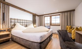 A modern hotel room with a large double bed and comfortable pillows. Bright colors and wooden details create a cozy atmosphere.