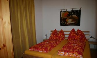 A cozy bedroom with a double bed and colorful cushions. The walls are painted in warm shades, and a piece of art hangs on the wall.