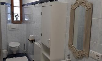 A modern bathroom with blue tiles, a sink, and a toilet. There is also an elegant mirror and a narrow cabinet.