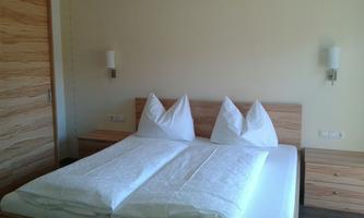 A cozy bedroom with a double bed and two pillows. The walls are light, and the wooden furniture looks modern.