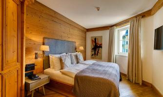 A cozy bedroom with wooden-paneled walls and a large double bed. The modern lamps and the television give the room an inviting atmosphere.