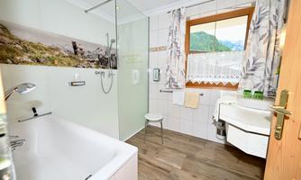 A modern bathroom with a bathtub and a shower. The room has large windows that offer a view of the mountains.