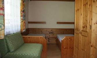 A simple room with two beds and a green couch. The walls are made of wood, and there is plenty of natural light through the window.