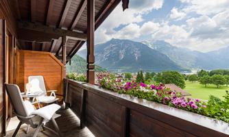 A balcony with two chairs and blooming plants. In the background, majestic mountains and a clear sky can be seen.