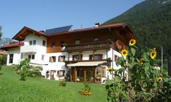 A beautiful house with a garden full of sunflowers. In the background, mountains and a clear sky can be seen.