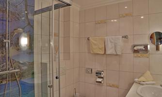 A modern bathroom with a shower cabin and bright tiles. Towels are hanging on the wall, and in the background, a picturesque wall design can be seen.