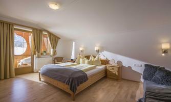 A bright bedroom with wood paneling and large windows. The room is cozily furnished and has a view outside.