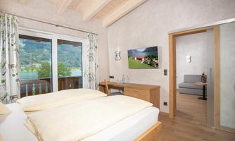 A cozy bedroom with a large bed and television. The windows offer a view of the surrounding nature.