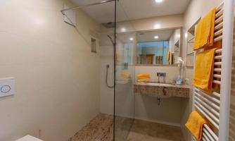 A modern bathroom with a glass shower and a stylish sink. Yellow towels provide a fresh accent.