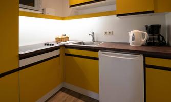 A modern kitchen with yellow cabinets and a functional setup. There is a sink, a refrigerator, and a coffee machine.