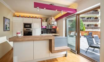 Modern kitchen with a wooden base and elegant appliances. Large windows offer a view of an outdoor area with loungers.