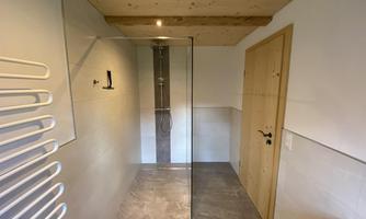 A modern bathroom with a glass shower and a dark tiled floor. The walls are in neutral tones, and there is a wooden ceiling covering.