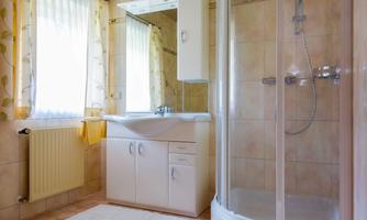 A bright bathroom with a shower and a sink. Large windows let in plenty of light.