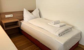 A simple bedroom with a single bed. There are fresh bed linens and towels on the mattress.