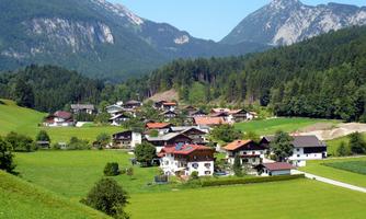 A picturesque village view with traditional houses amidst green meadows. In the background, majestic mountains rise under a clear sky.