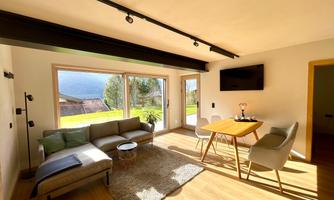A bright living room with a modern sofa and a table. Large windows offer a view to the outside and plenty of natural light.