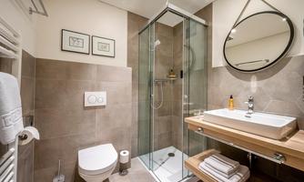 A modern bathroom with a glass shower and a wall mirror. On the wooden shelf, there is a sink with personal care products.