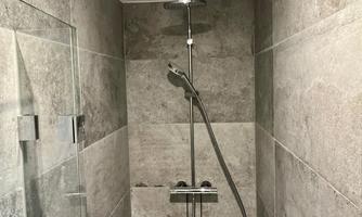 A modern shower with gray tiles and a handheld showerhead. The shower is spacious and well-lit.