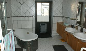 A modern bathroom with a bathtub and shower, two sinks, and large tiles. There is a window that lets in natural light.
