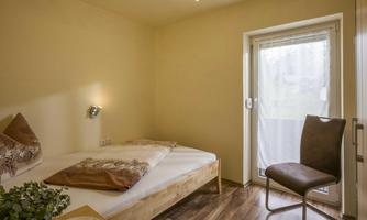 A simple room with a bed and a chair. The room has a window that opens to nature.