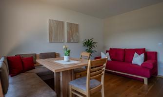 A cozy living area with a red sofa and a wooden table. Two pictures hang on the wall and a green plant is on the table.